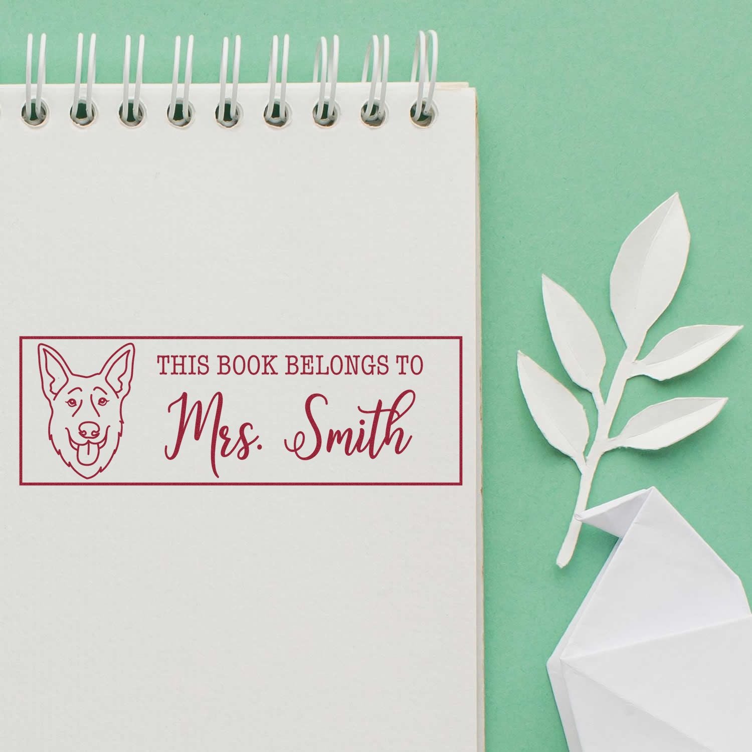 Custom rubber stamp book label with dog illustration and This Book Belongs to Mrs. Smith in a spiral notebook.