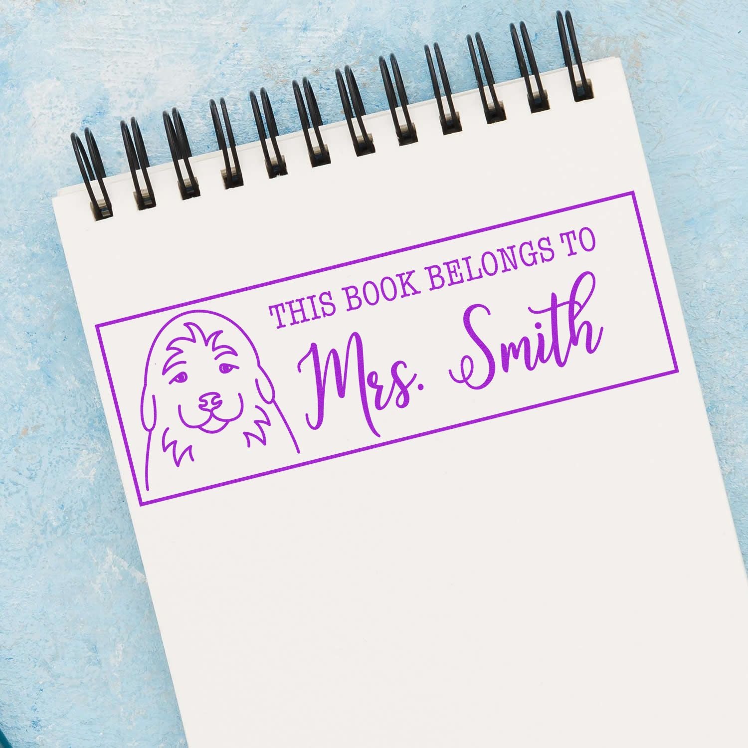 Personalized rubber book stamp with dog design reading This Book Belongs to Mrs. Smith in purple ink.