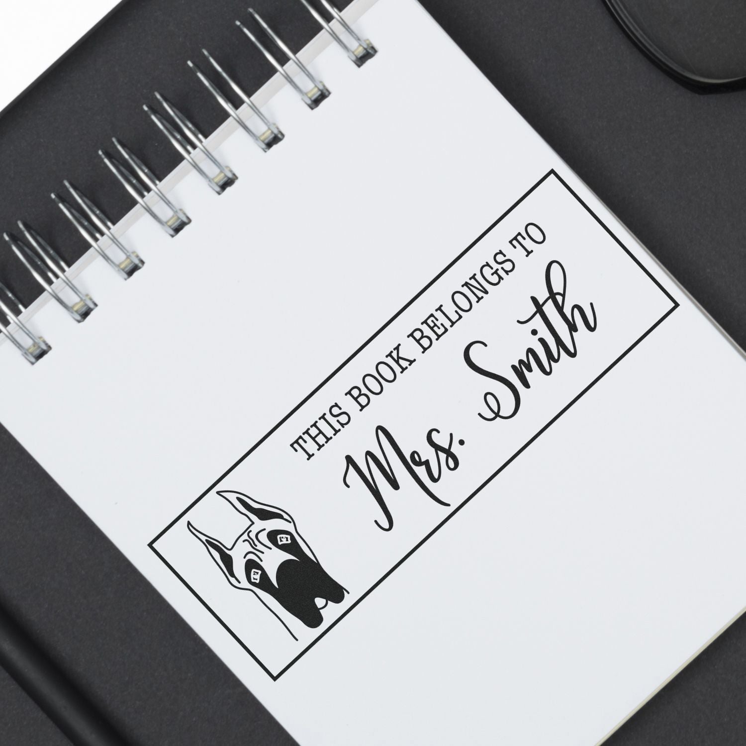Custom rubber stamp design reading This Book Belongs to Mrs. Smith with dog illustration for personalized book labeling.