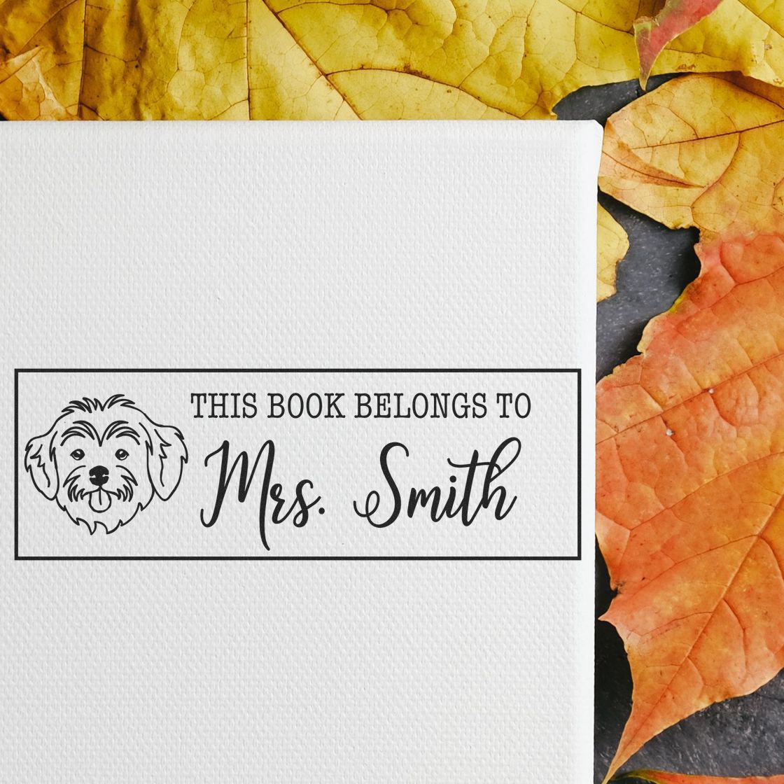 Custom rubber stamp bookplate with dog icon and This Book Belongs to Mrs. Smith on textured paper with fall leaves.