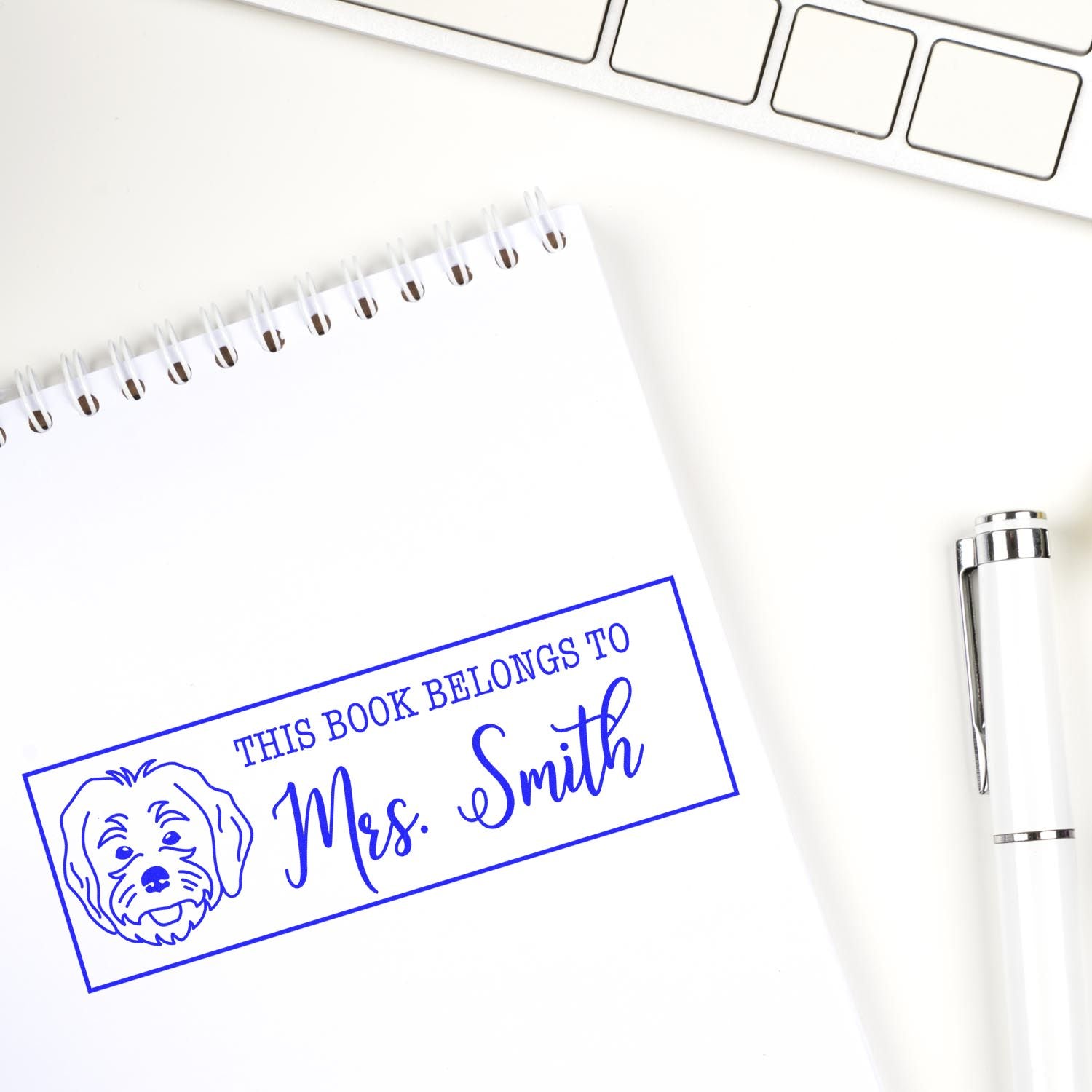 Personalized rubber book stamp for Mrs. Smith with dog design on notebook, plus pen and keyboard on desk.