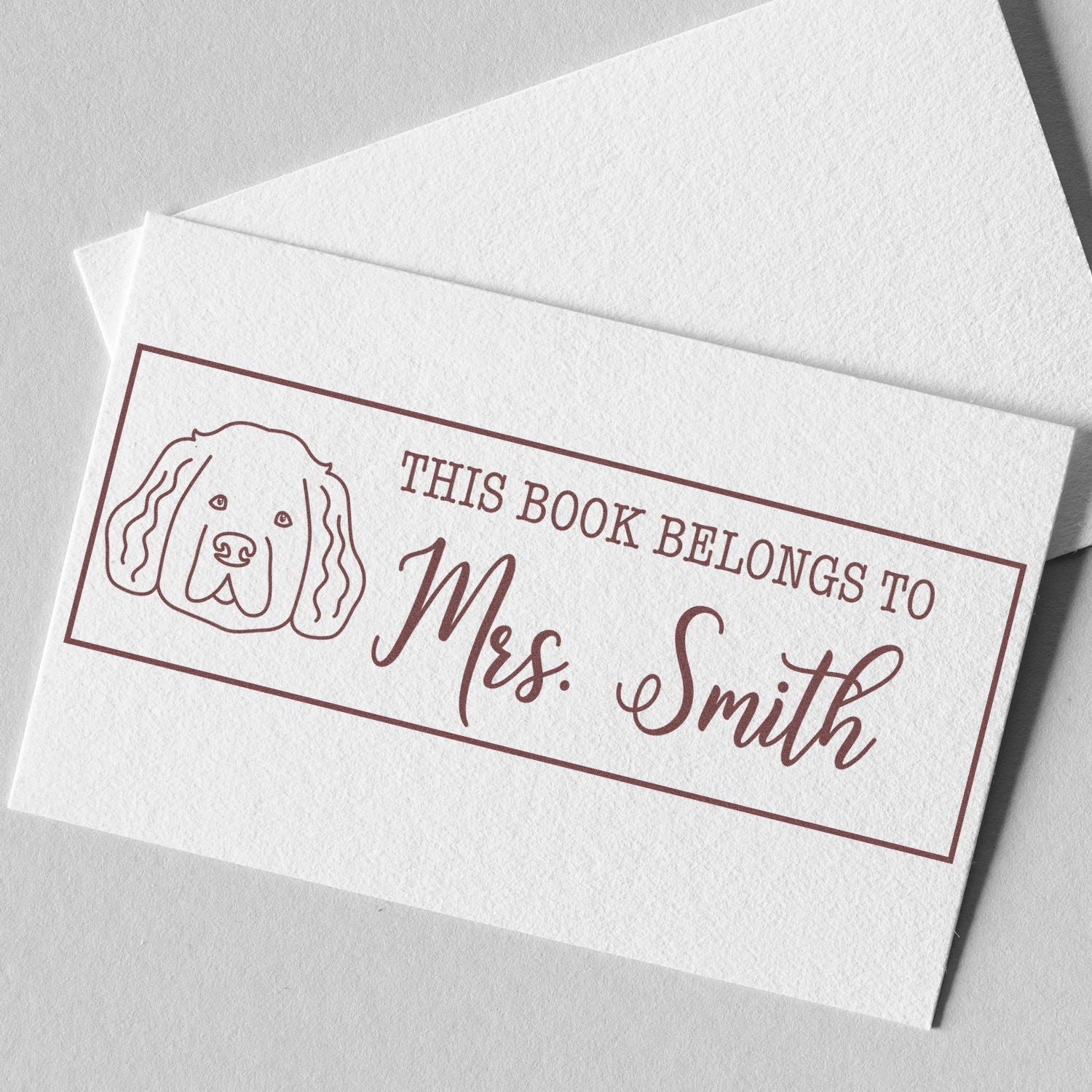 Personalized rubber book stamp with dog illustration and This Book Belongs to Mrs. Smith text for custom bookplates.