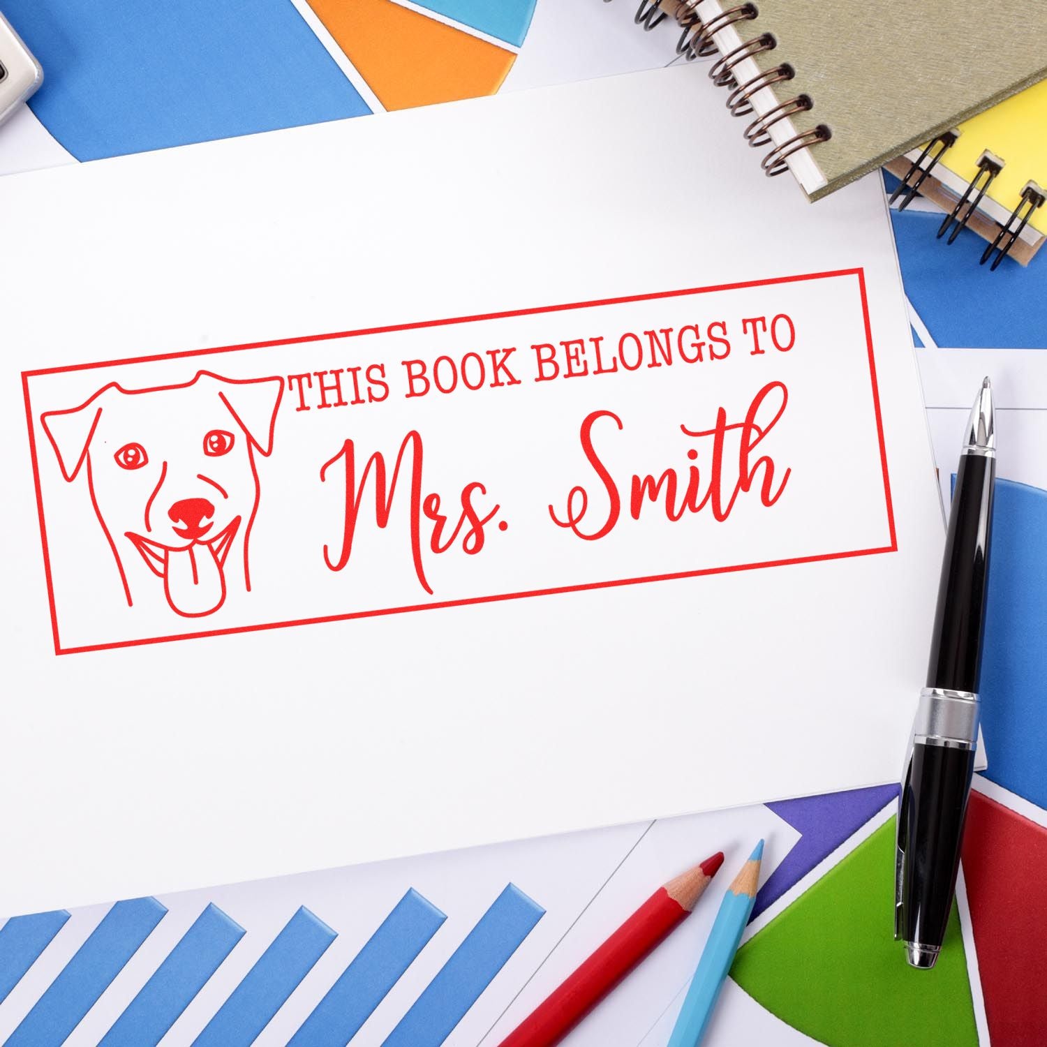 Personalized rubber book stamp with dog icon reading This Book Belongs to Mrs. Smith on stationery background.