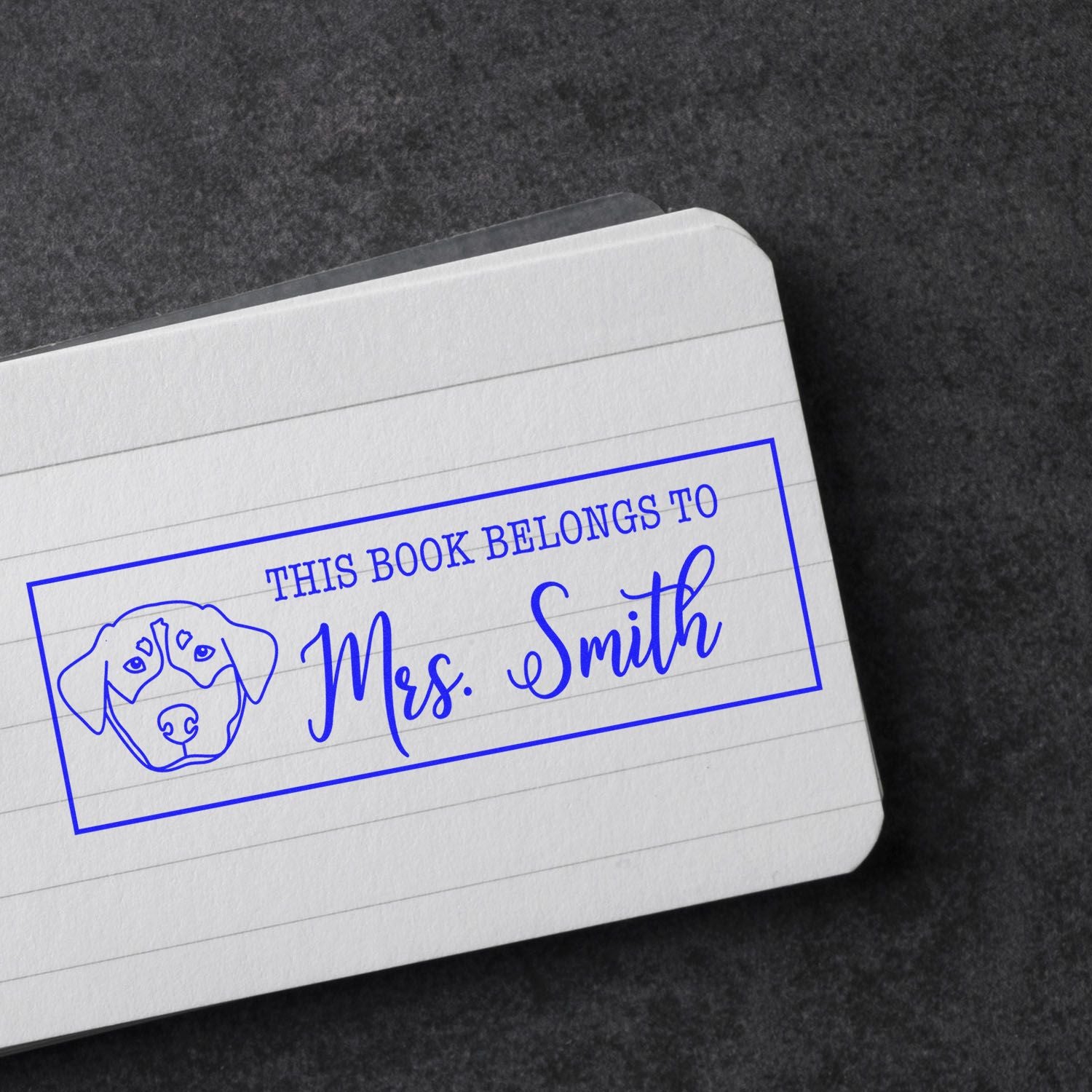 Custom rubber stamp bookplate with dog illustration and This Book Belongs to Mrs. Smith on lined paper.