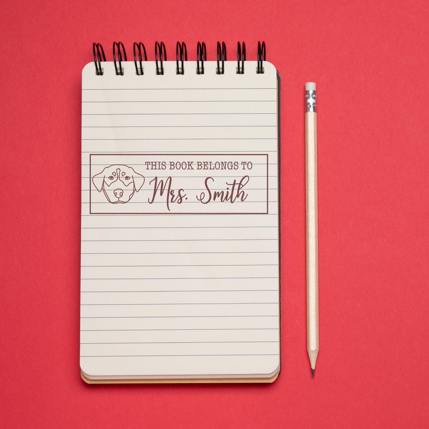 Personalized rubber book stamp with dog icon, labeling a notebook This Book Belongs to Mrs. Smith for books and stationery