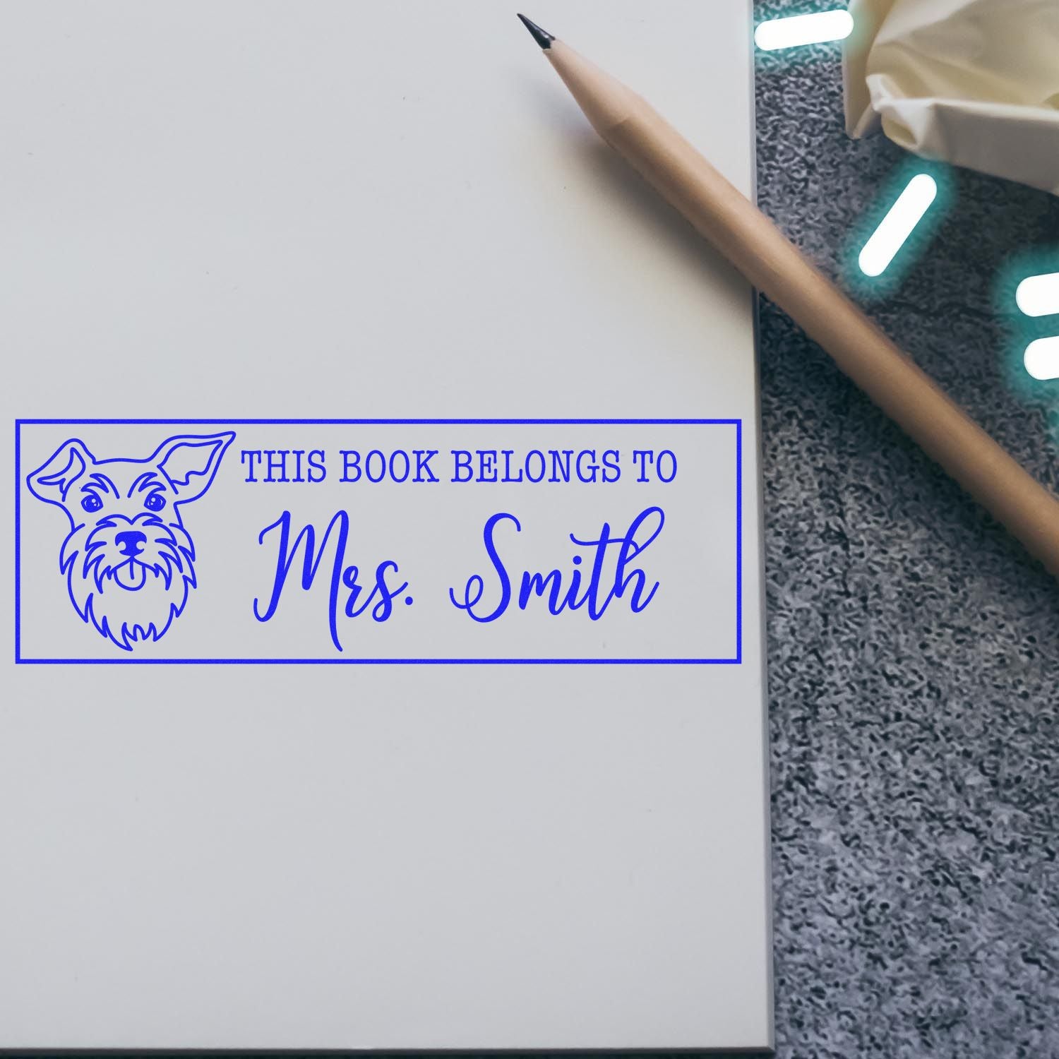 Custom rubber book stamp with dog design reading This Book Belongs to Mrs. Smith on a book page.