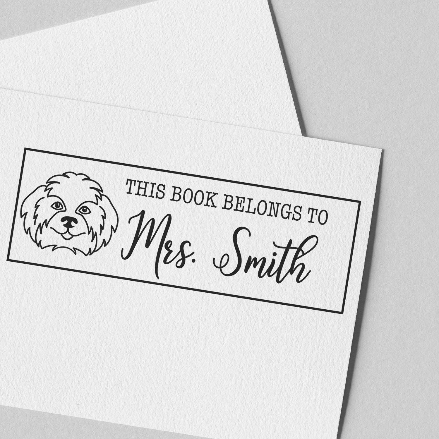 Personalized rubber book stamp with dog illustration and This Book Belongs to Mrs. Smith for custom library labeling.