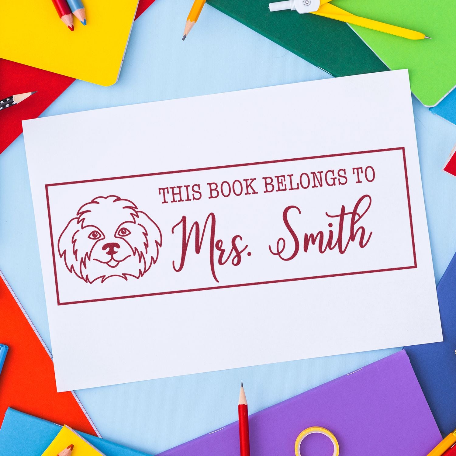 Custom rubber book stamp reading This Book Belongs to Mrs. Smith with dog illustration on colorful stationery background.