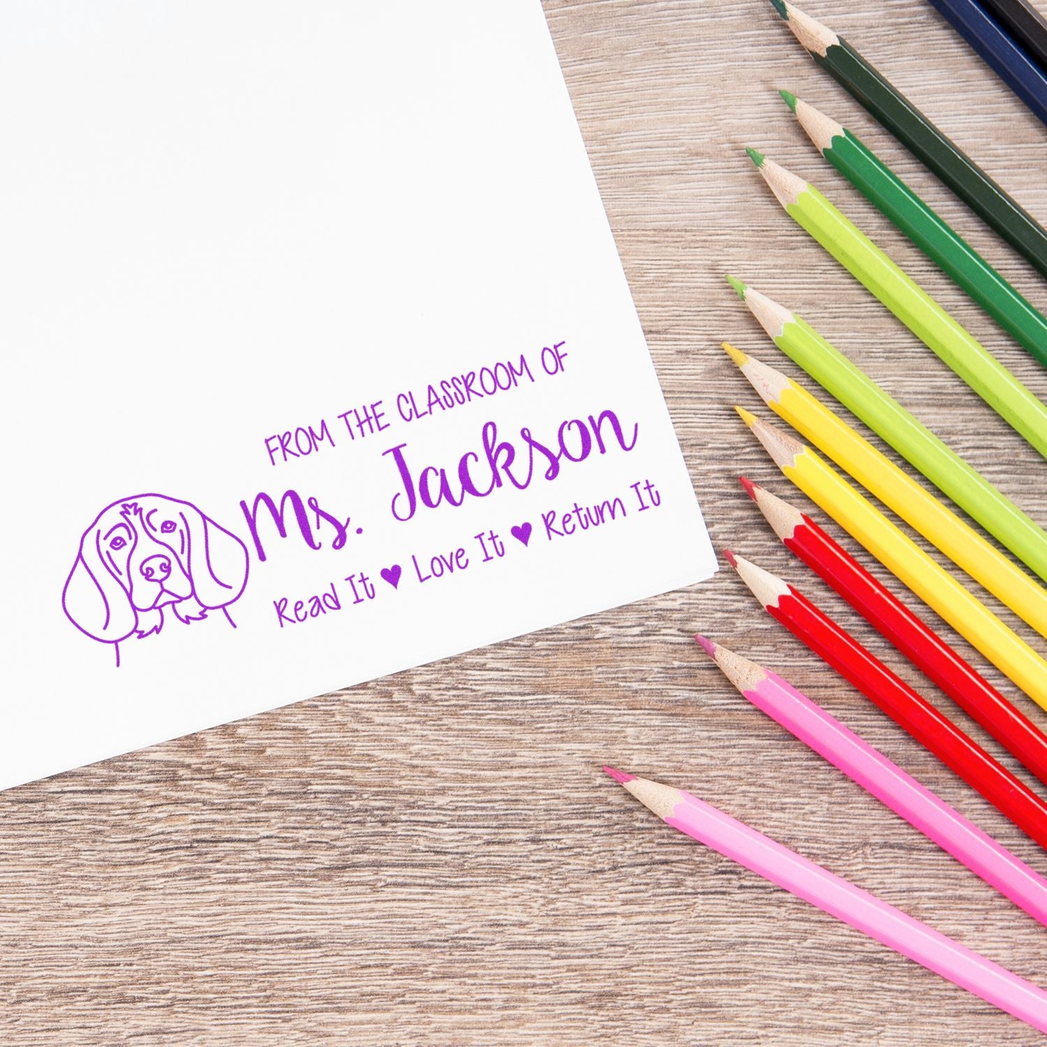 Custom classroom rubber stamp for Mrs. Jackson, stamped on paper beside colored pencils, with Read It, Love It, Return It message.