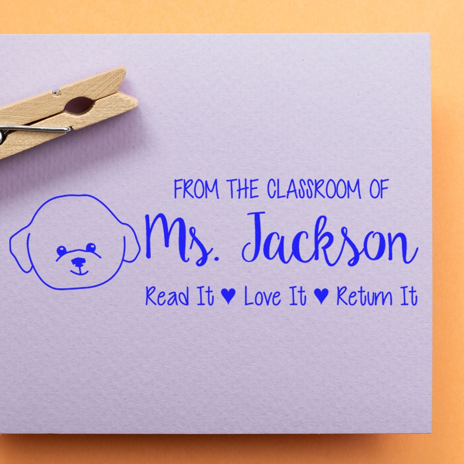 Personalized classroom rubber stamp for Ms. Jackson with dog icon and Read It, Love It, Return It message on paper.