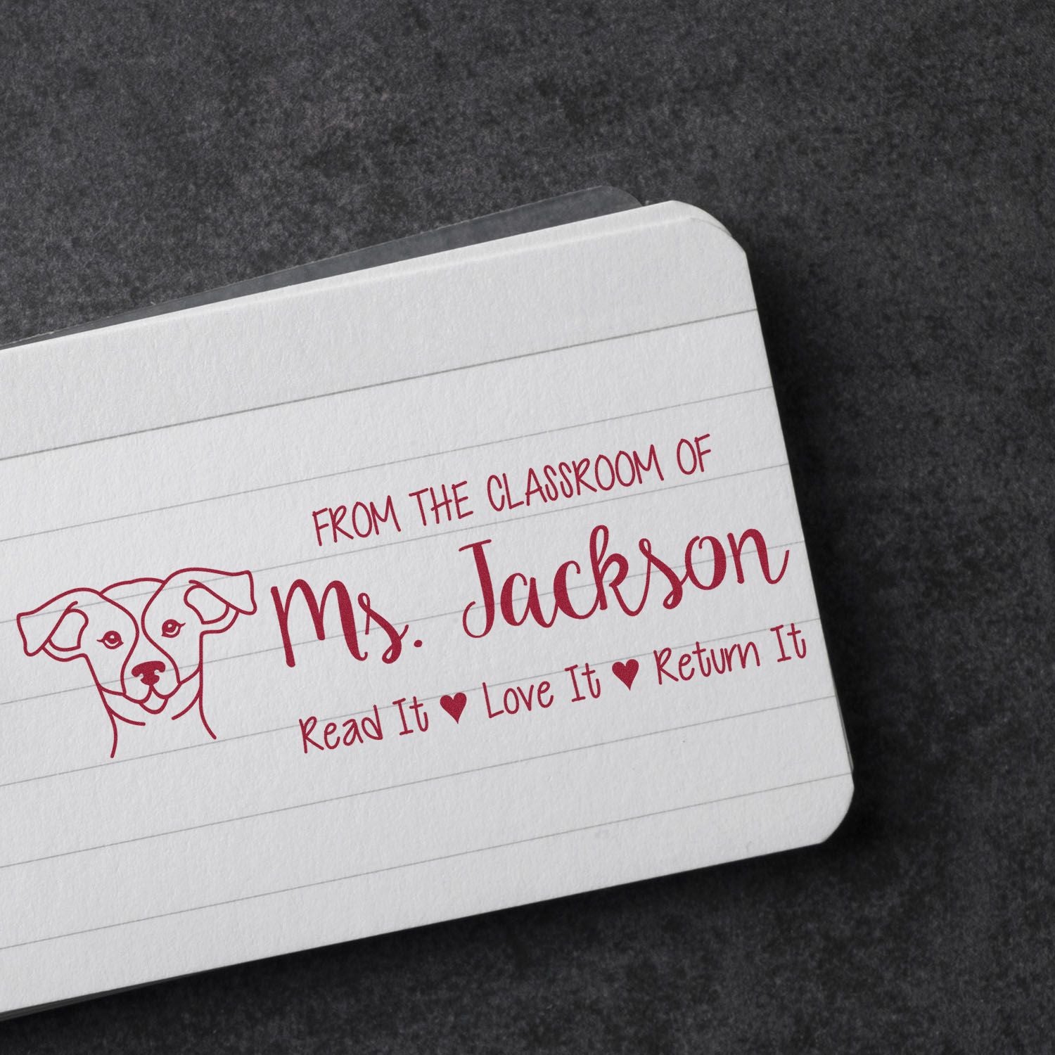 Custom teacher rubber stamp on notebook reading From the classroom of Ms. Jackson with Read it, Love it, Return it and dog icon.