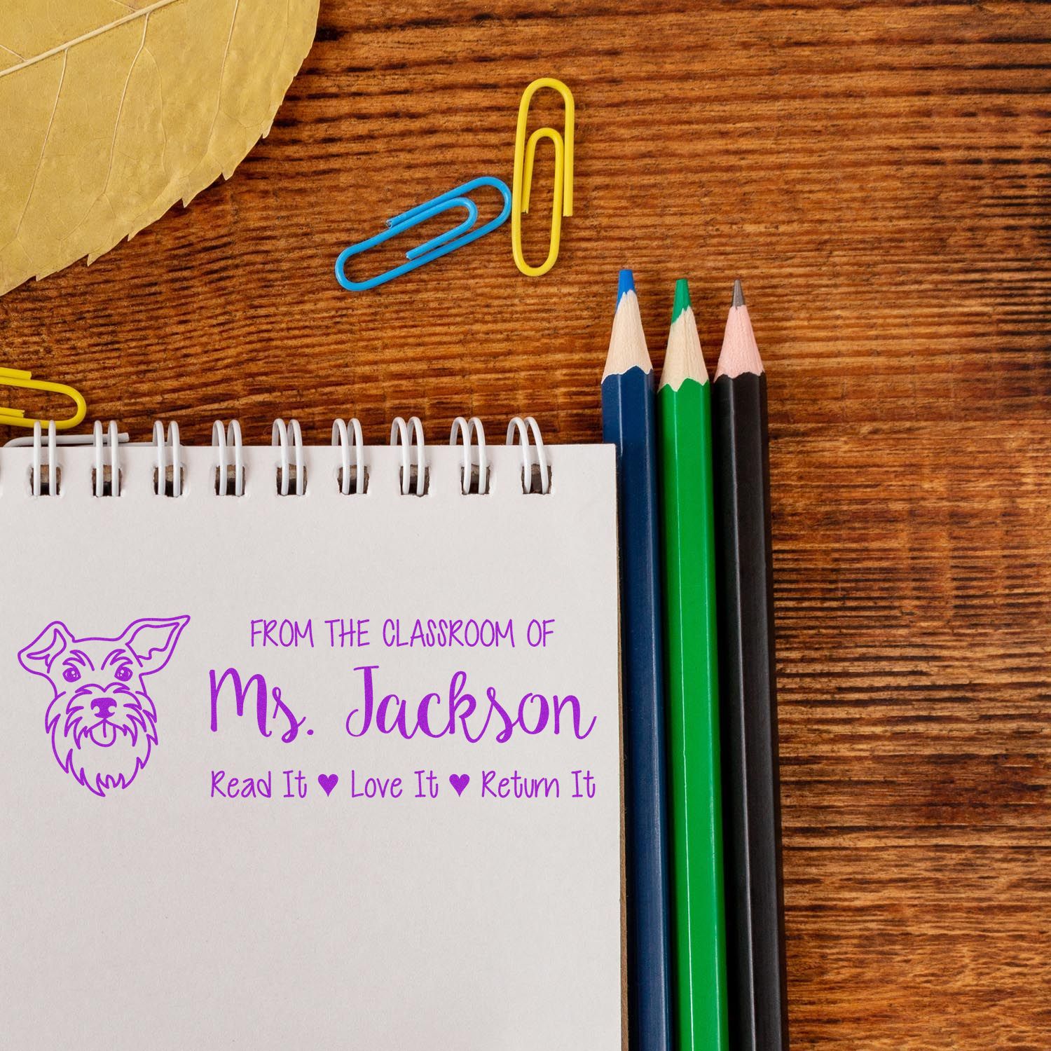 Custom teacher rubber stamp on notebook reading From the classroom of Ms. JacksonRead It, Love It, Return It with dog icon.
