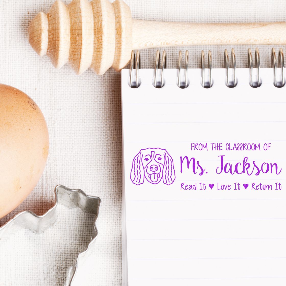 Custom classroom rubber stamp on notebook reads From the Classroom of Ms. Jackson with dog icon and Read It Love It Return It.