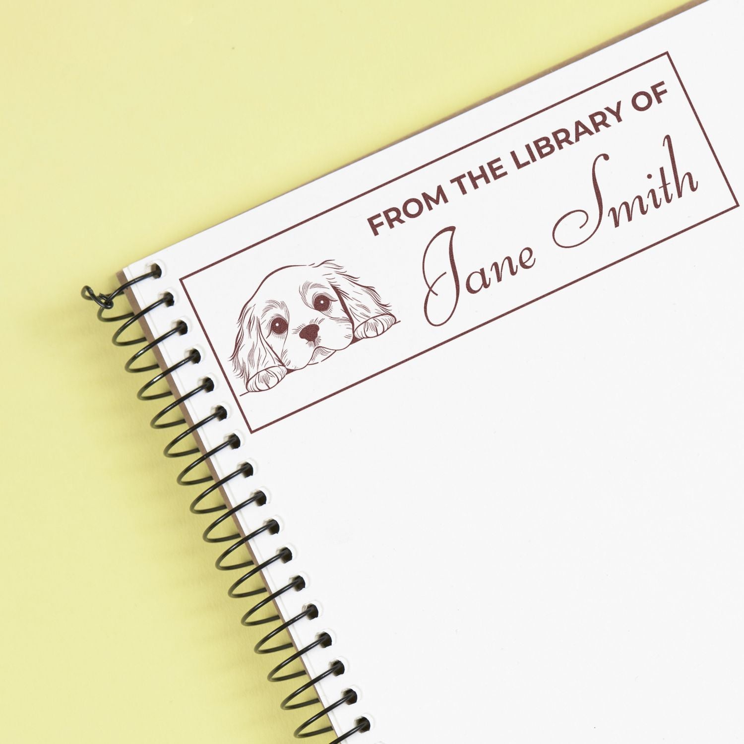 Personalized rubber book stamp reading From the Library of Jane Smith with a dog illustration on a notebook.