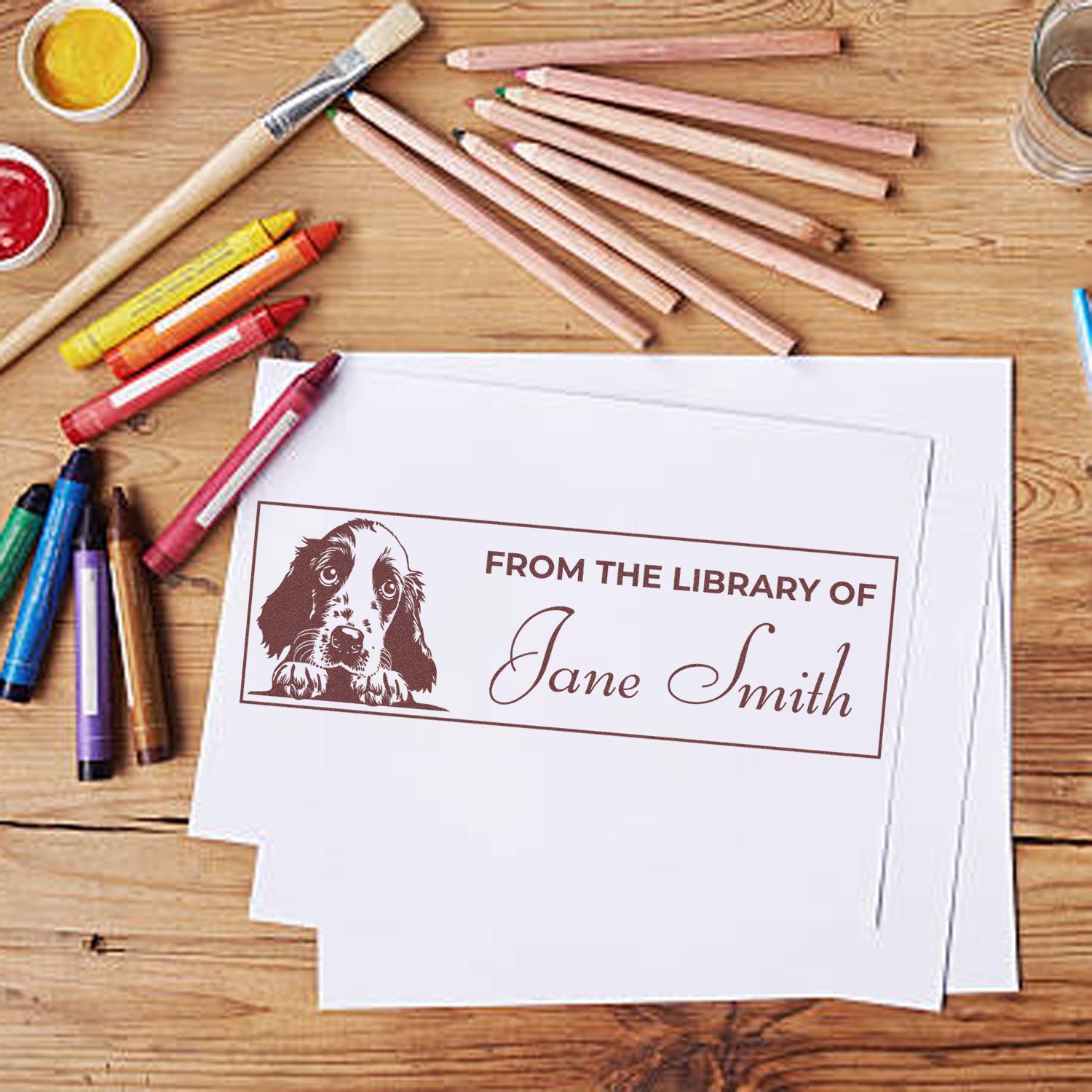 Custom "From the Library of" rubber stamp with dog illustration and name, stamped on paper for personalized books.