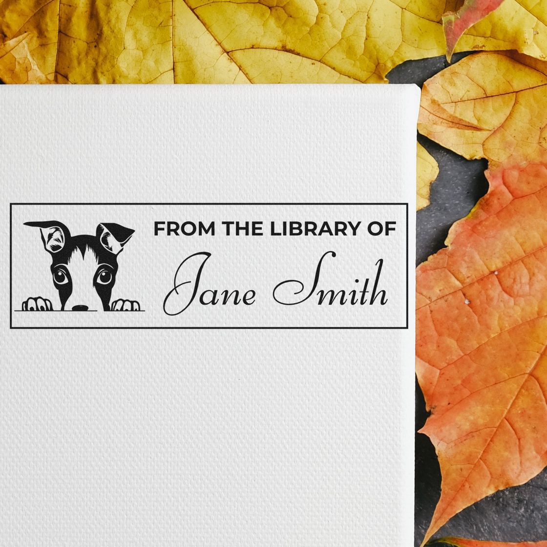 Custom rubber library stamp with dog design reading From the Library of Jane Smith on white paper with autumn leaves.