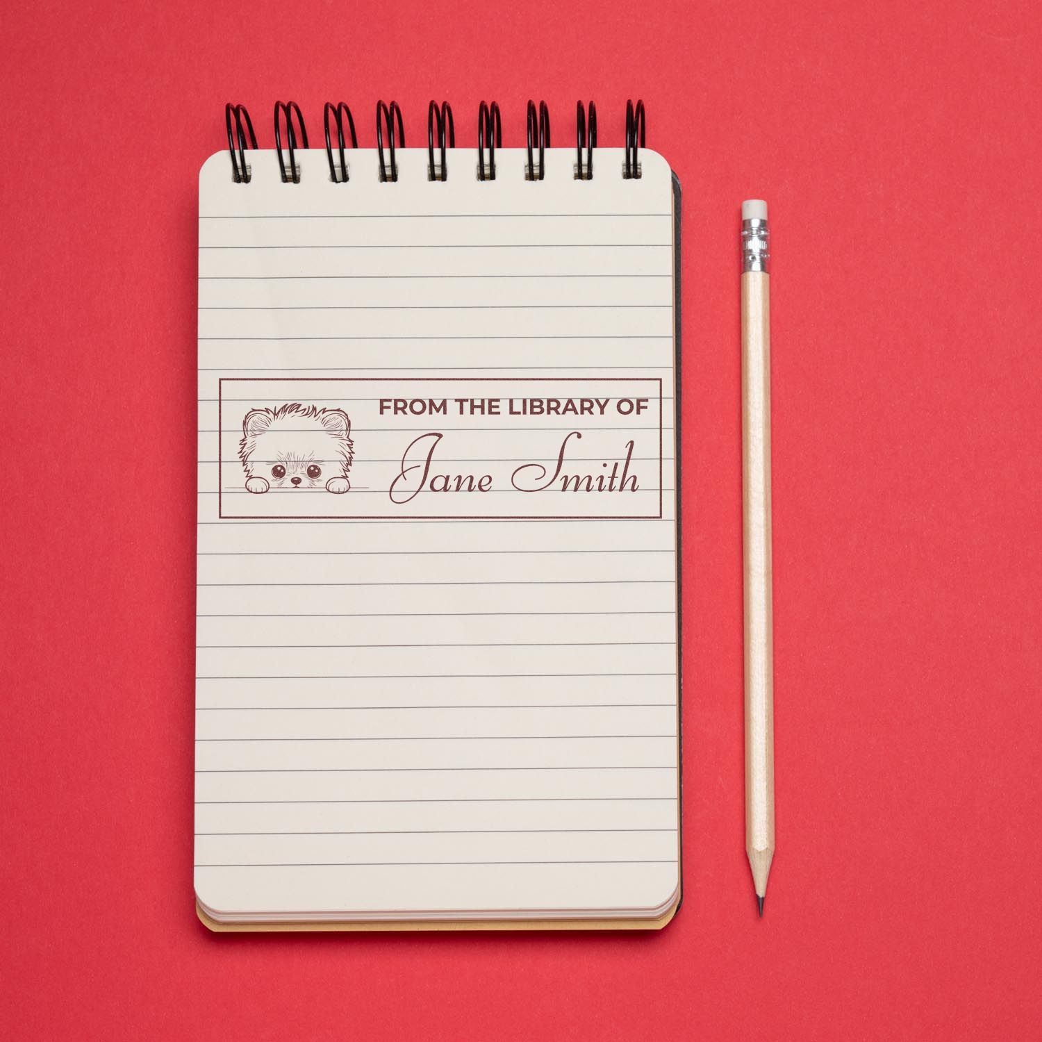 Custom library rubber stamp with From the Library of Jane Smith design on lined notebook beside pencil