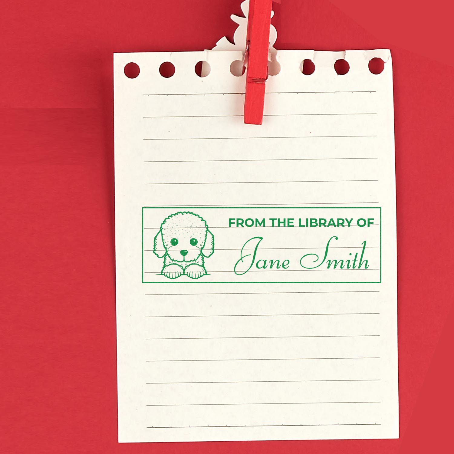 Personalized rubber stamp reading From the Library of Jane Smith with dog design on lined paper clipped to a red background.