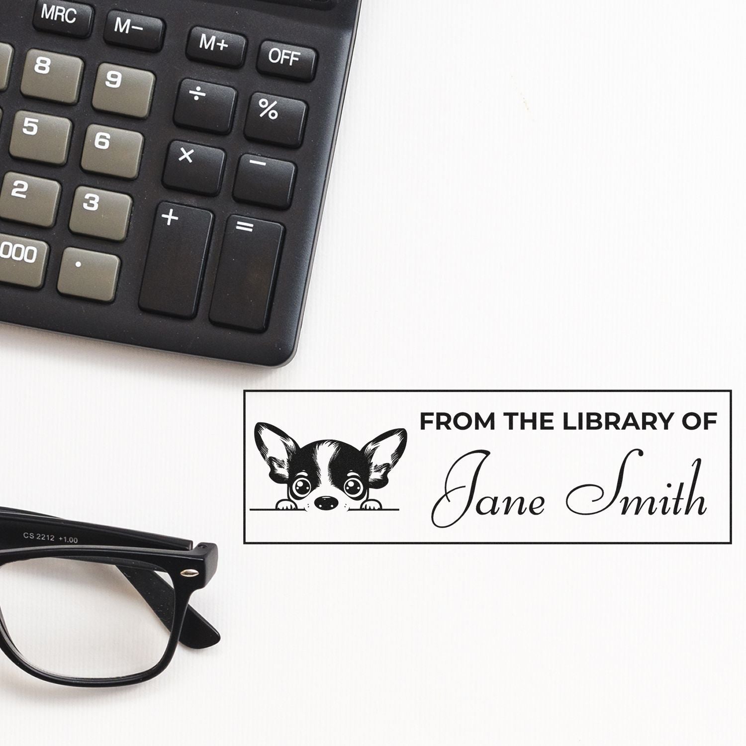 Custom rubber stamp for books: From the Library of Jane Smith with dog illustration, shown beside a calculator and eyeglasses.