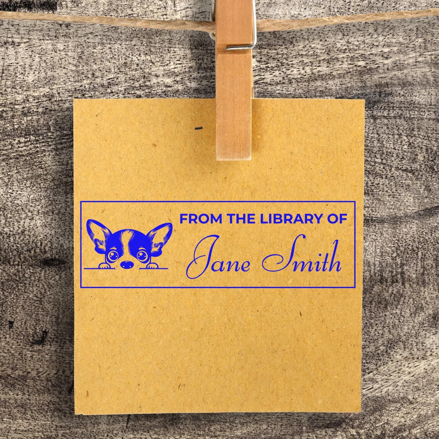 Custom rubber stamp for books reading From the Library of Jane Smith with dog graphic on kraft paper, clipped with clothespin.