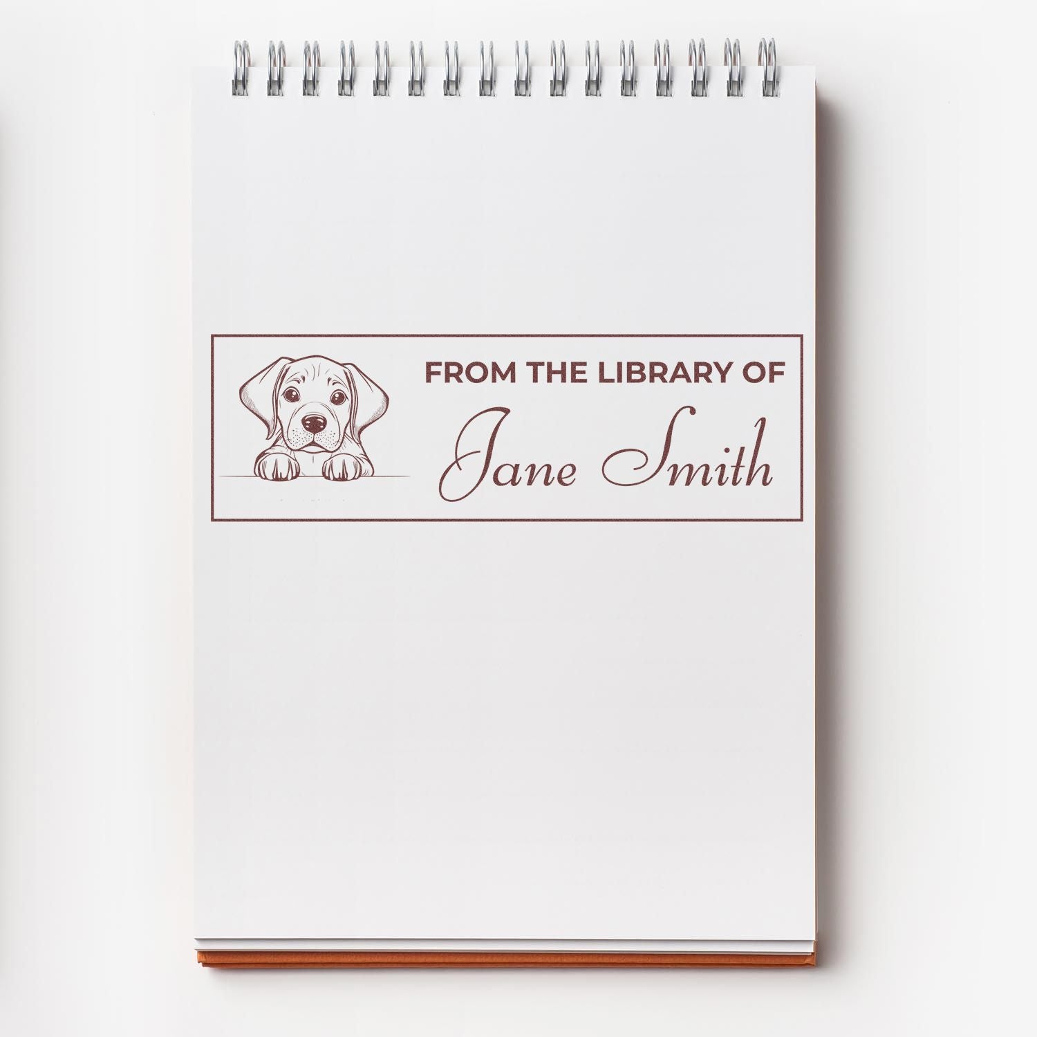 Custom library rubber stamp with puppy icon and From the Library of Jane Smith personalized bookplate on notebook.