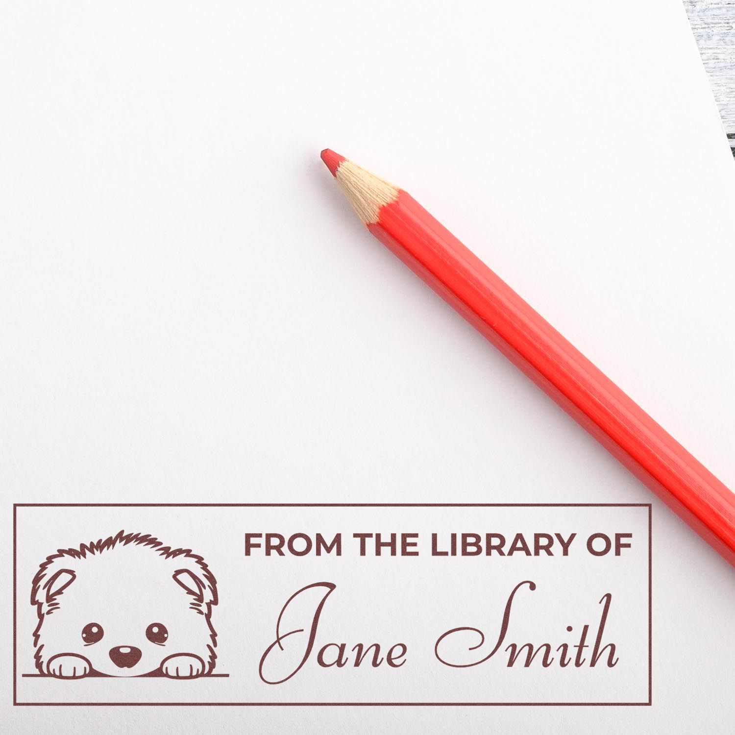 Personalized rubber library stamp with puppy design and From the Library of Jane Smith imprint beside a red pencil.