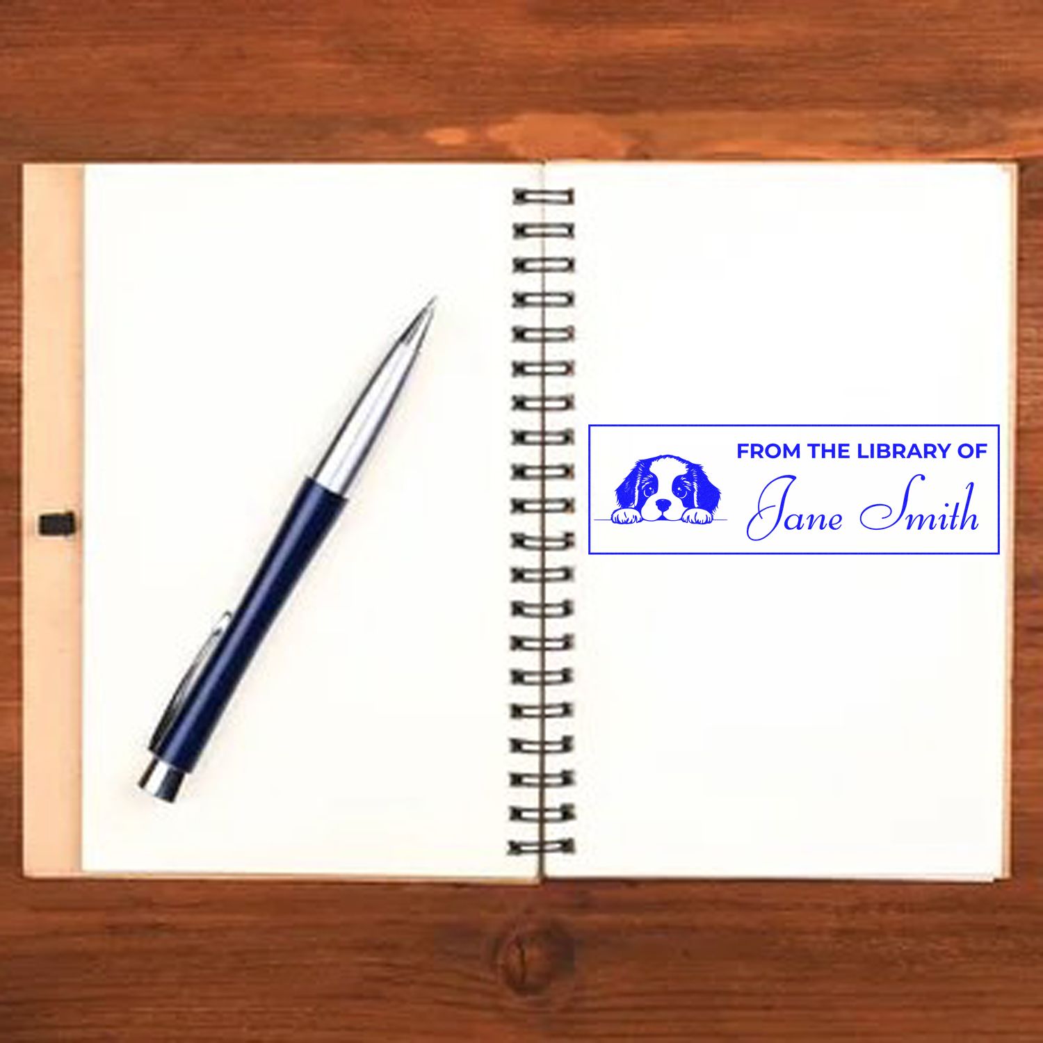 Personalized rubber stamp for books reading From the Library of Jane Smith with dog icon on an open notebook.