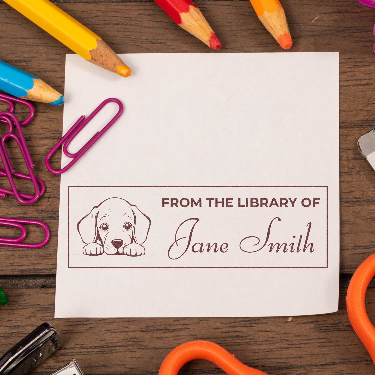 Personalized library rubber stamp with dog illustration and name Jane Smith, displayed on a note card with colorful school supplies.