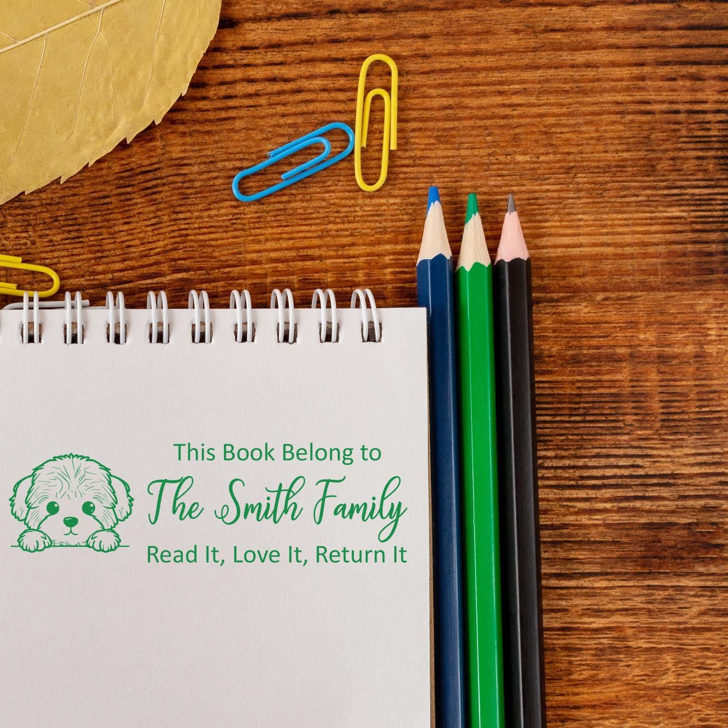 Personalized rubber book stamp with dog design reading This Book Belongs to The Smith Family on a notebook.