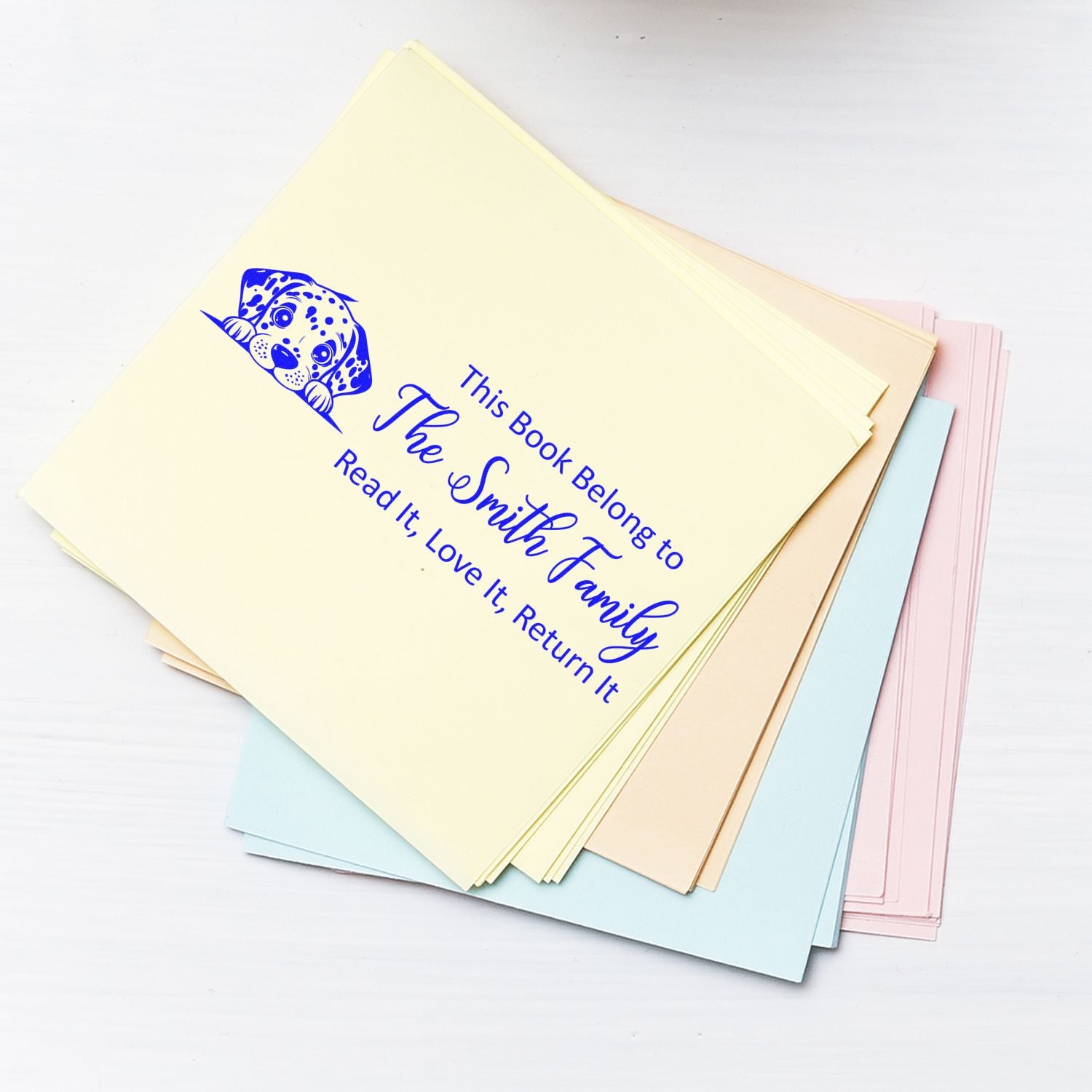 Personalized rubber book stamp with puppy art and This Book Belongs to The Smith Family text on pastel library cards.