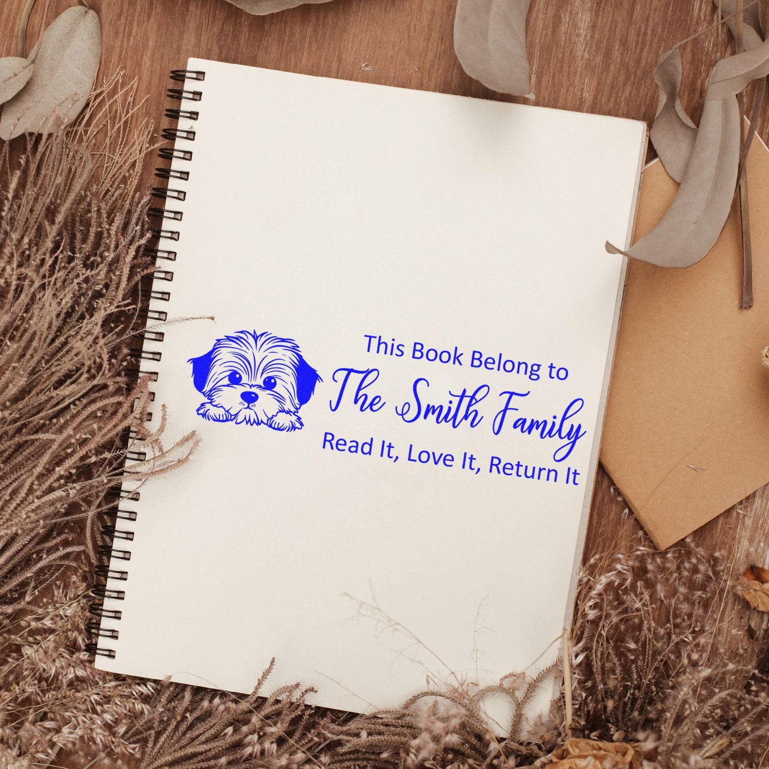 Personalized dog book rubber stamp: "This Book Belongs to The Smith Family, Read It, Love It, Return It" on a spiral notebook.