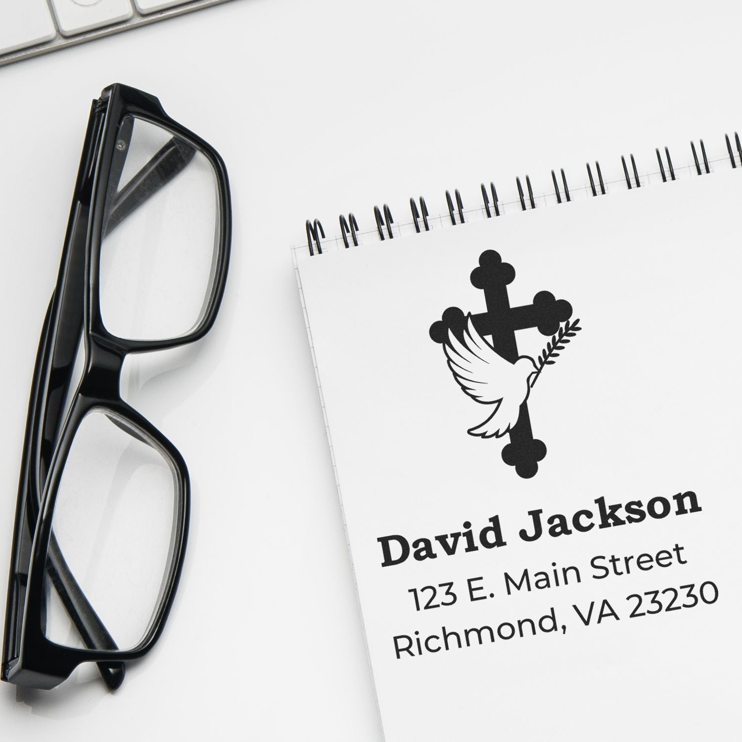 Custom rubber stamp with dove and cross logo, personalized address stamp for David Jackson, shown on a notepad beside eyeglasses.
