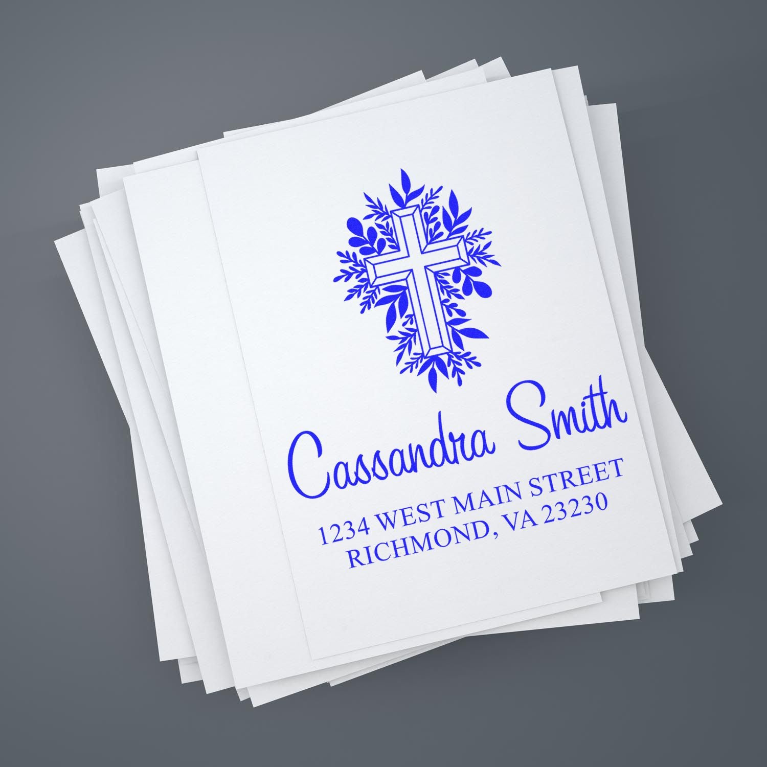 Custom church return address rubber stamp with floral cross, Cassandra Smith name, and Richmond, VA address on paper stack.
