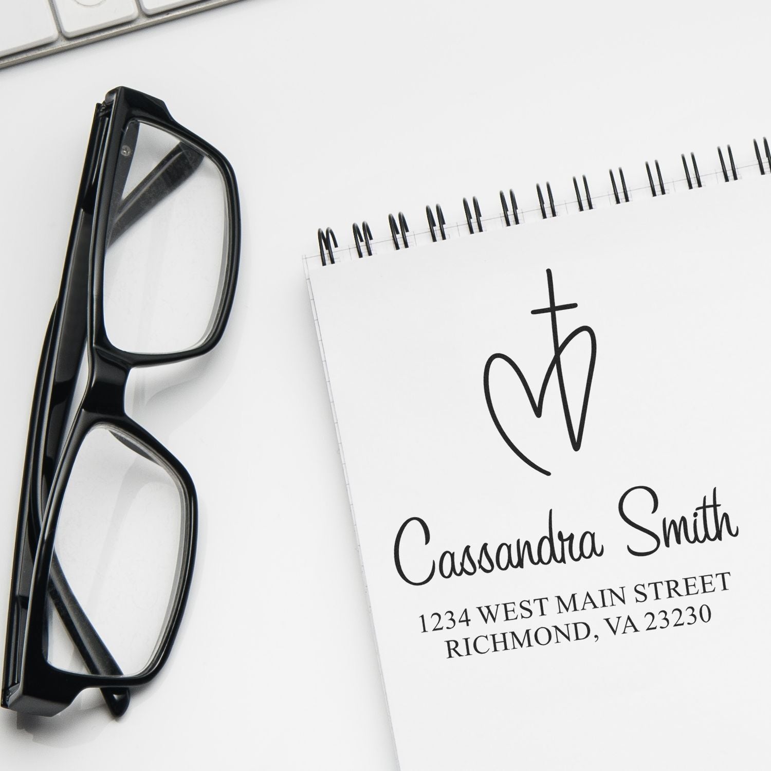 Personalized return address rubber stamp with monogram, name, and address on a notepad beside eyeglasses.