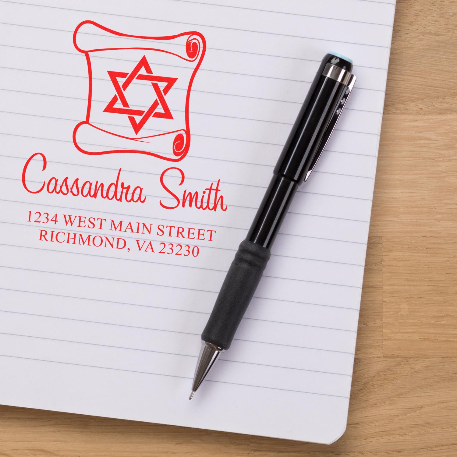 Personalized return address rubber stamp imprint with name and address on notebook beside a pen
