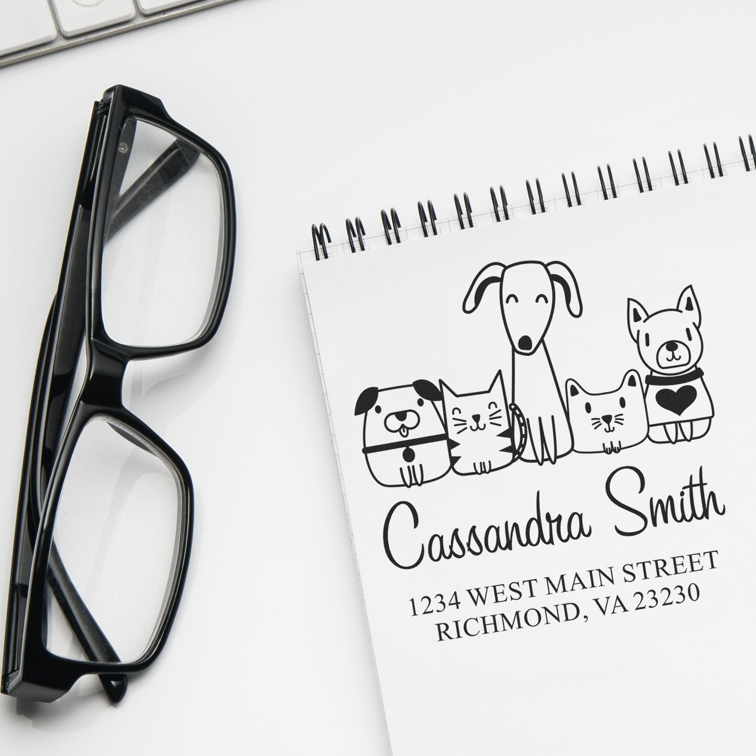 Personalized rubber return address stamp with dog and cat design on notebook, beside black eyeglasses.