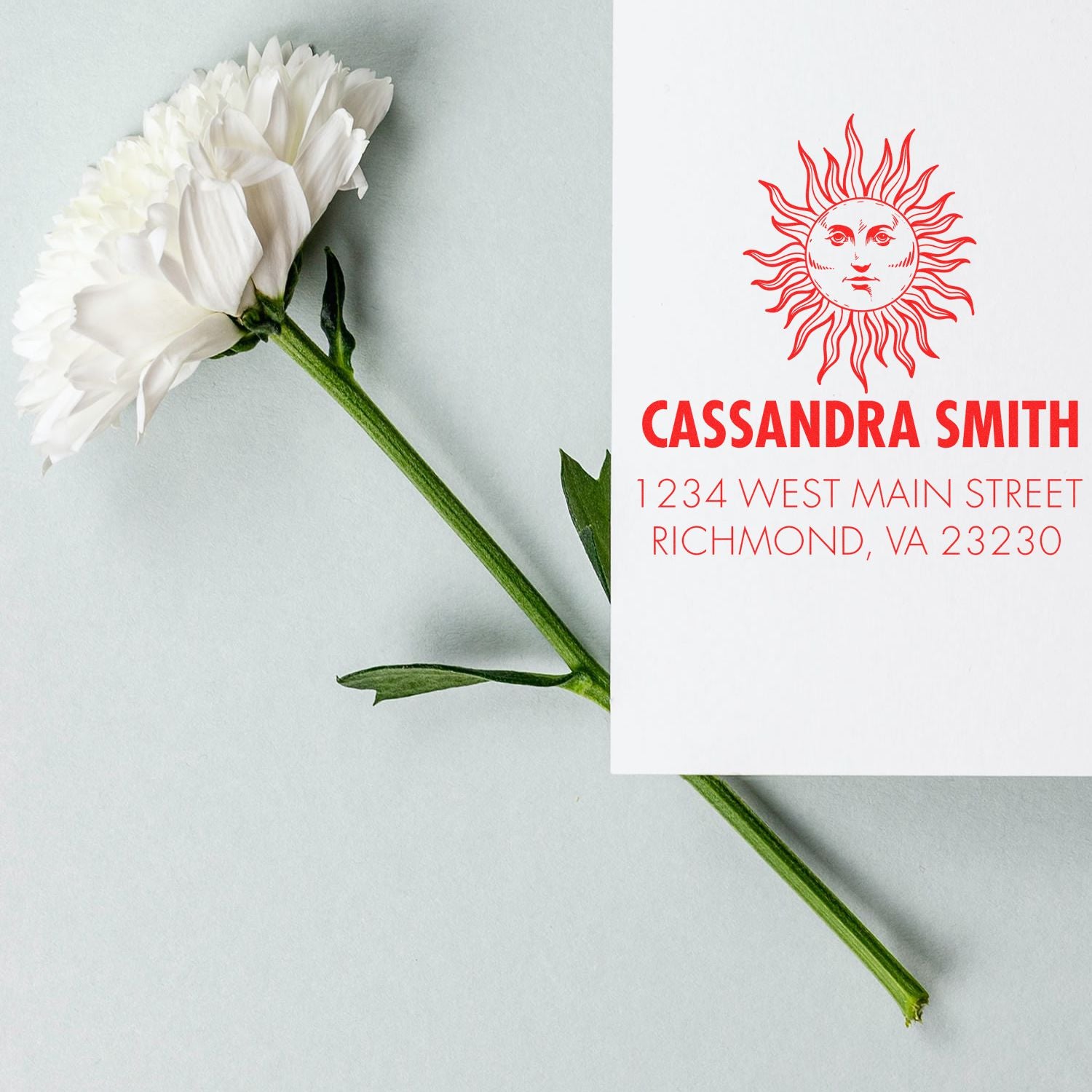 Custom return address rubber stamp with sun logo, Cassandra Smith name, and Richmond, VA address on a floral flat lay.