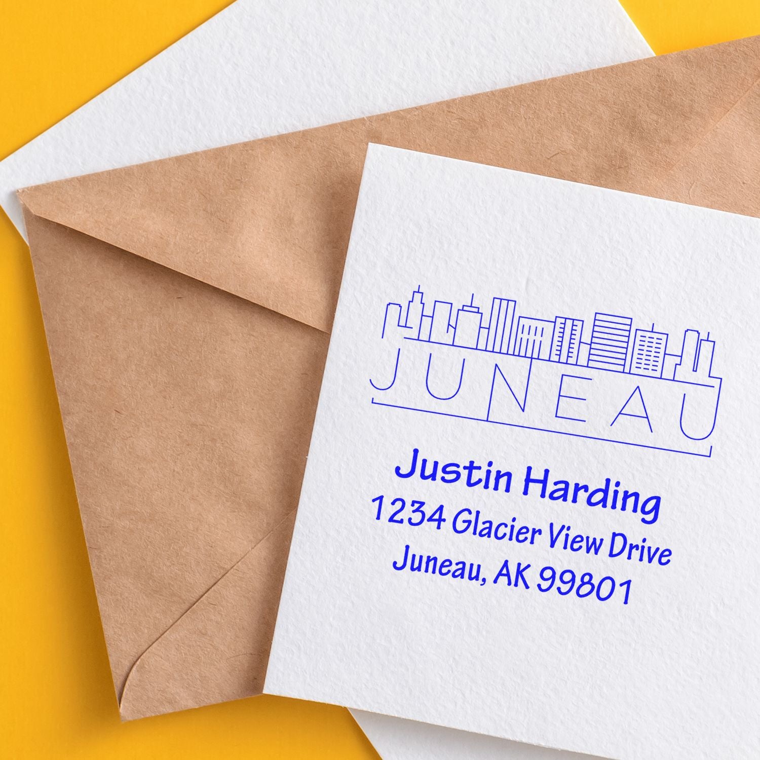 Custom return address rubber stamp on envelope with Juneau skyline logo and blue ink, personalized mailing address design