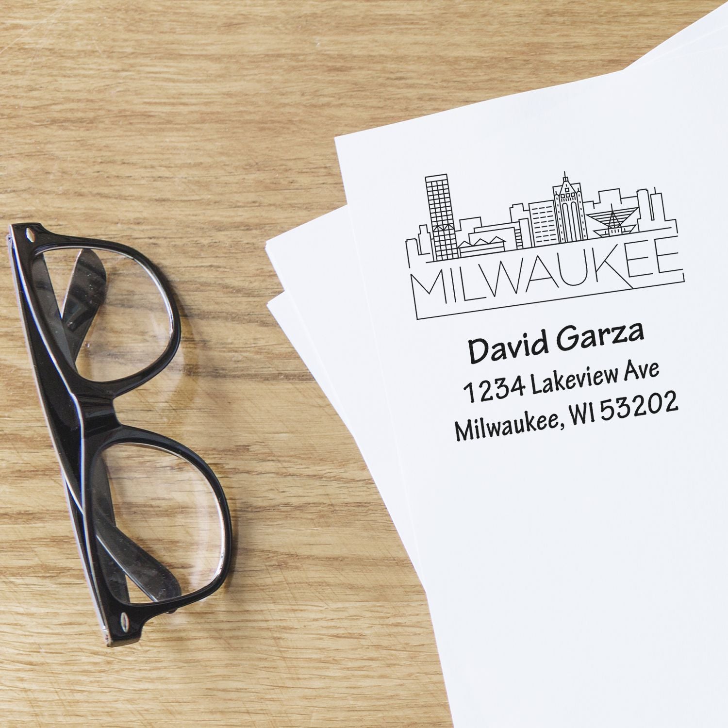Custom Milwaukee address rubber stamp sample with skyline design, shown on paper beside eyeglasses.