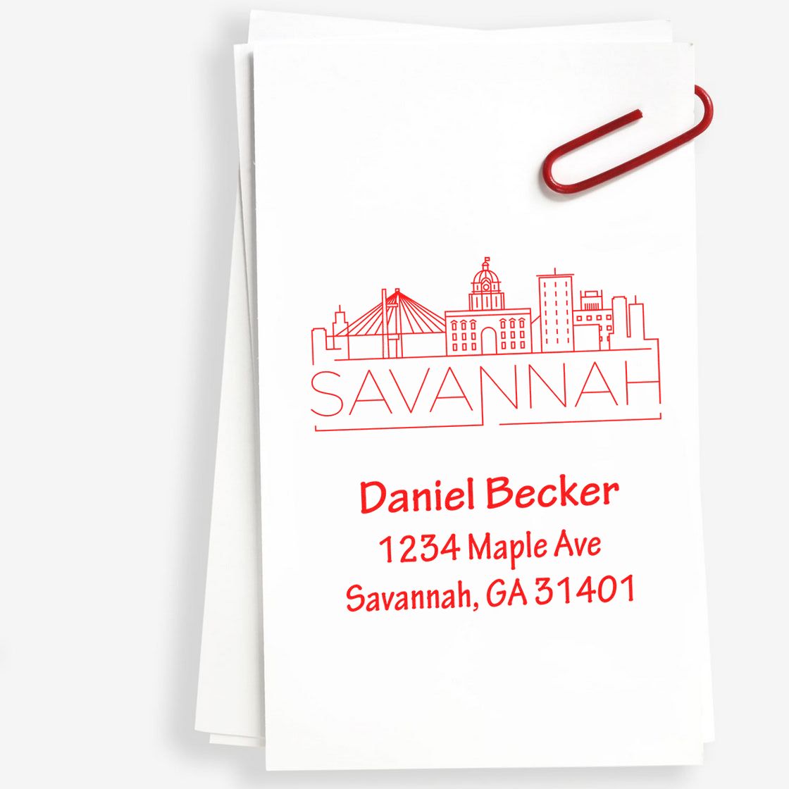 Personalized rubber address stamp on white stationery with Savannah skyline, Daniel Becker return address, and red paper clip.