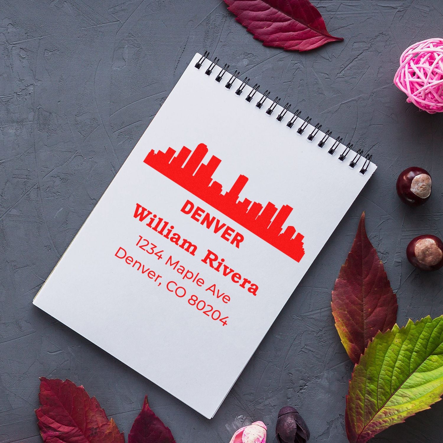 Custom Denver address rubber stamp on notebook, featuring skyline logo and return address for William Rivera, 1234 Maple Ave, Denver, CO 80204.