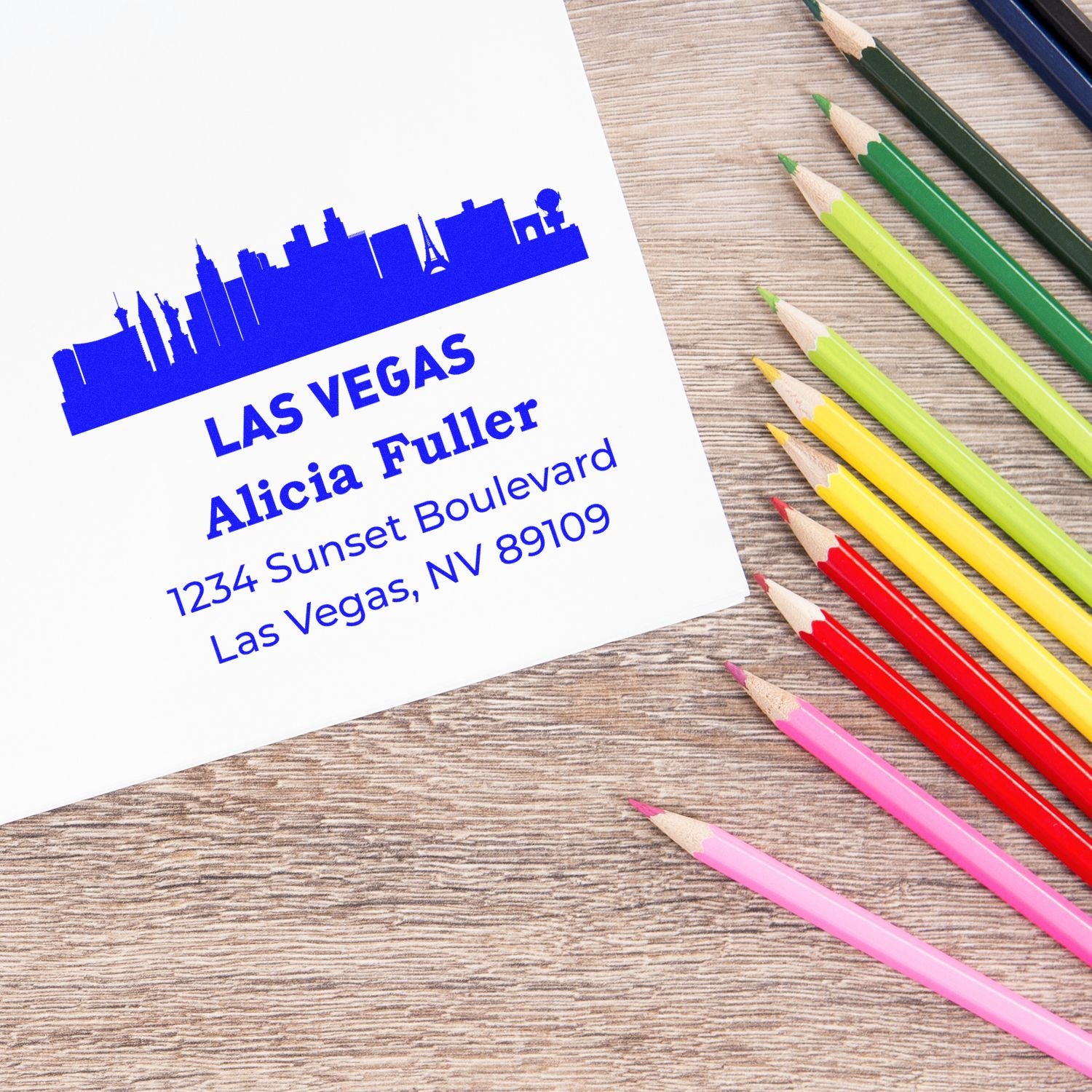Custom return address rubber stamp with Las Vegas skyline, name, street address, and colorful pencils on a wood table.