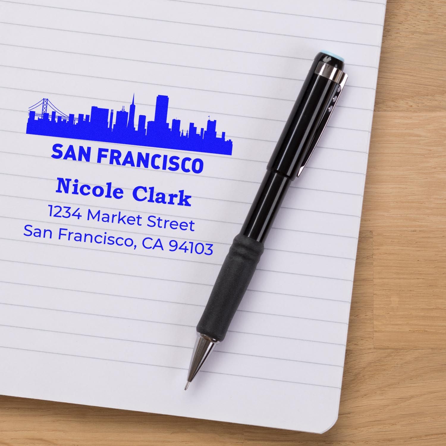 Custom self-inking rubber address stamp with San Francisco skyline, name, and address on notebook.
