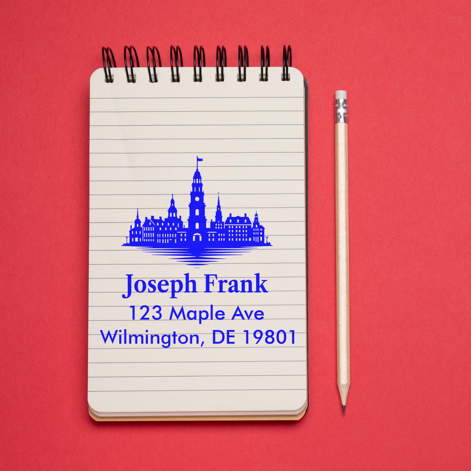 Custom address rubber stamp on notebook showing Joseph Frank, 123 Maple Ave, Wilmington, DE 19801, with skyline design.