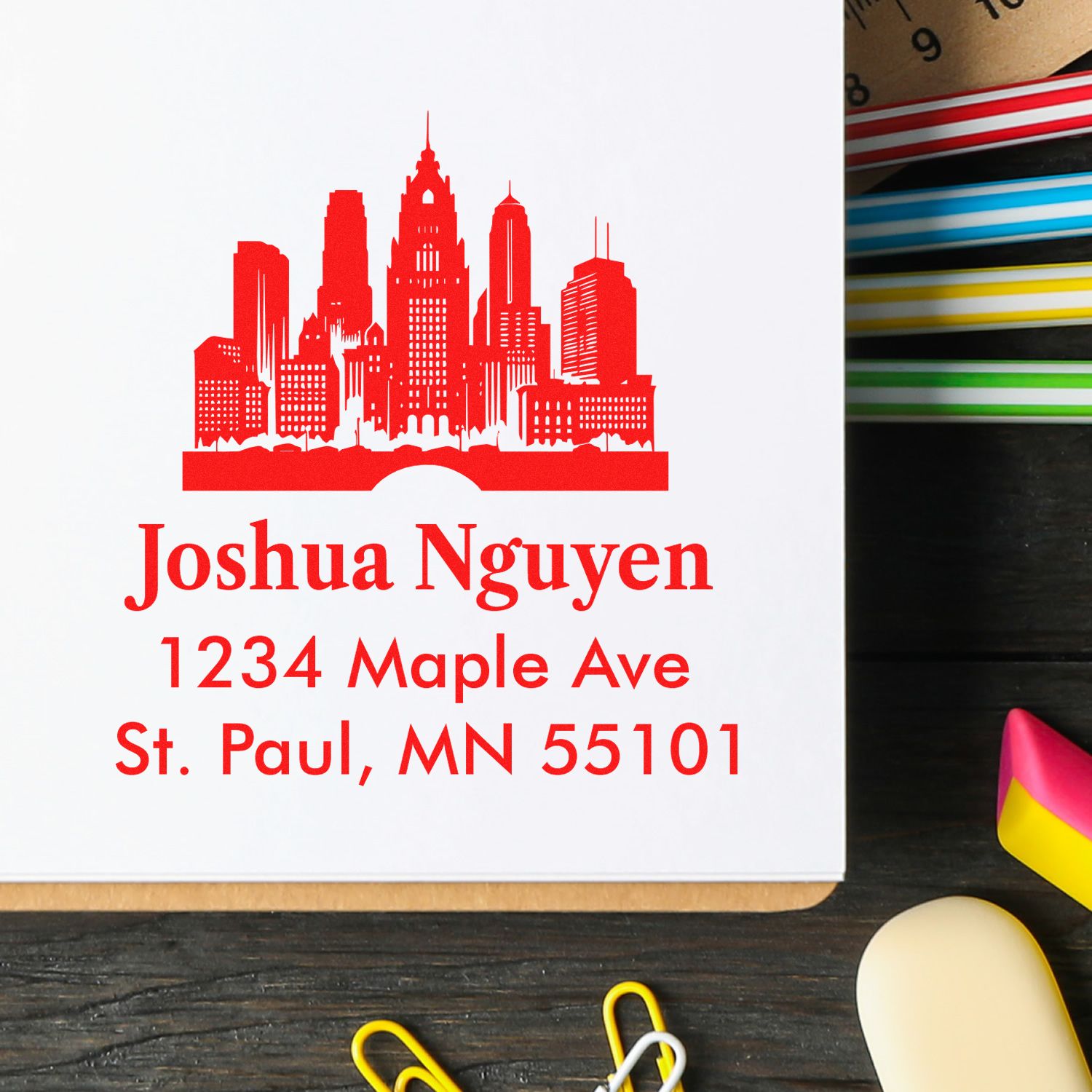 Custom skyline address rubber stamp with Joshua Nguyen, 1234 Maple Ave, St. Paul, MN 55101 in red ink.