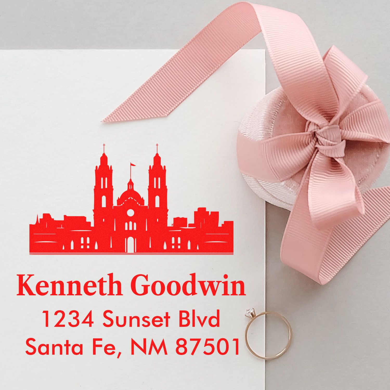Custom rubber stamp return address for wedding invitations, shown on an elegant envelope with pink ribbon and ring.