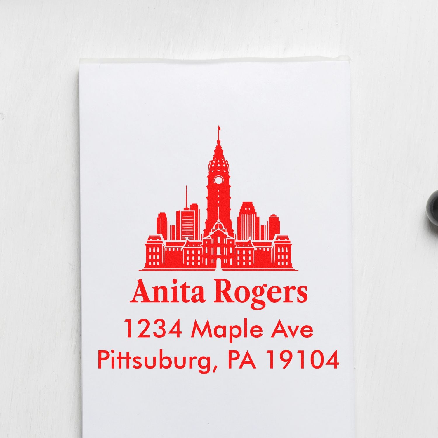Custom red address rubber stamp with skyline design for Anita Rogers, 1234 Maple Ave, Pittsburg, PA 19104.