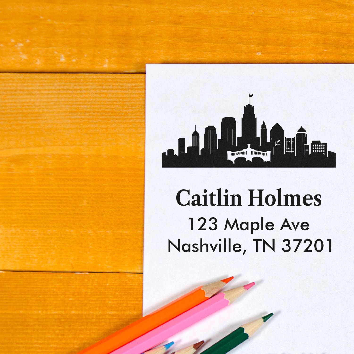 Custom Nashville return address rubber stamp with skyline design on white paper beside colored pencils.