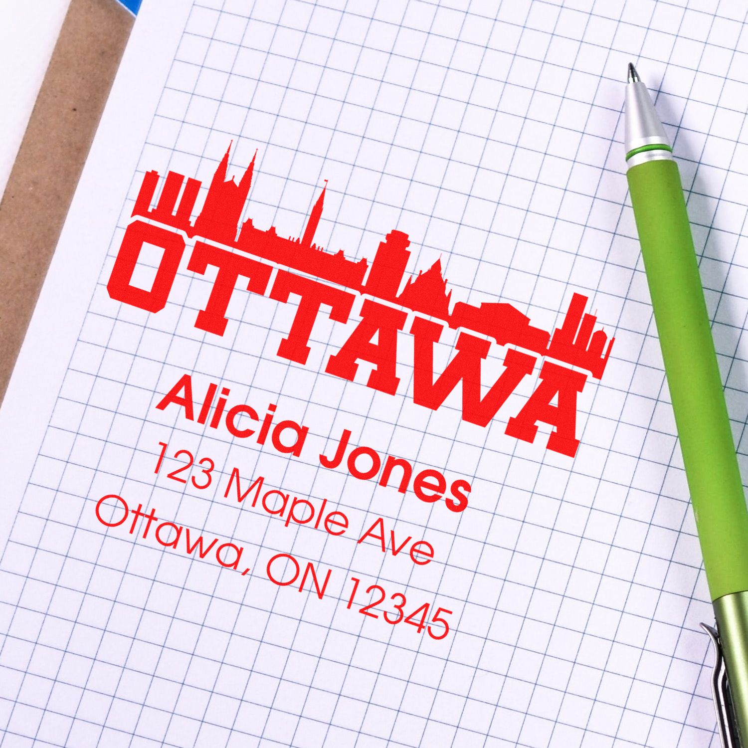 Custom Ottawa address rubber stamp with skyline, name, and mailing address design on graph paper next to a pen.