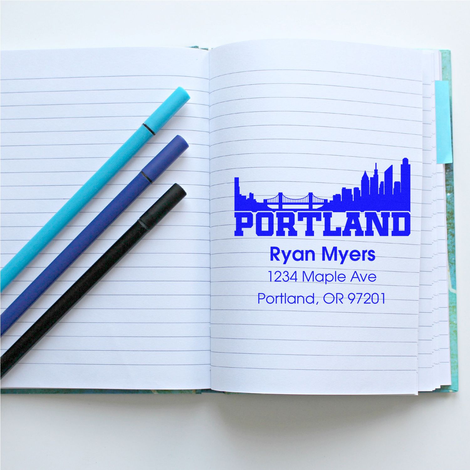 Custom Portland rubber stamp with skyline and address imprint on an open notebook beside pens
